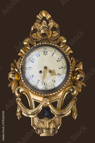 Old antique gold-plated wall clock isolated on a brown background