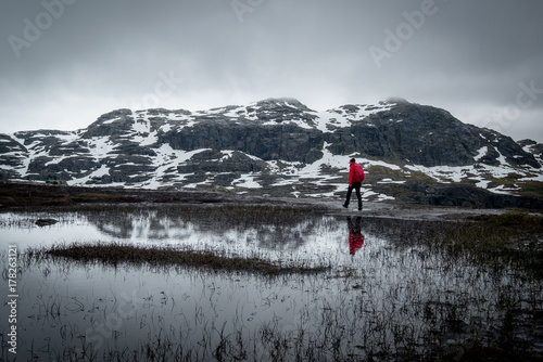 Female hiker in a red jacket hiking Trolltunga trail in middle of mountains. © 1tomm