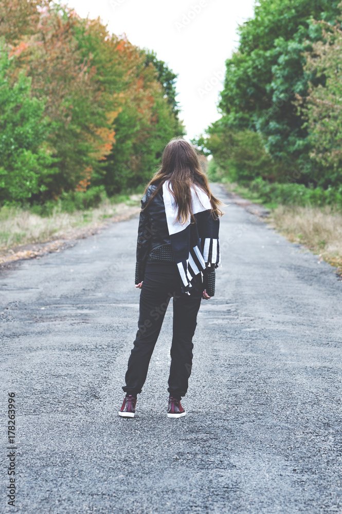 The vertical view of rear view of sad woman with scarf on the head near the empty forest road. Concept of waiting and sadness. Instagram filter The vertical view of rear view of sad woman with scarf on the head near the empty forest road. Concept of waiting and sadness. Instagram filter