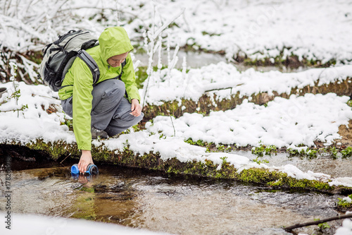 woman filling bottle of water from a winter forest stream.