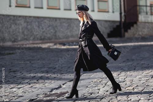 Fashion woman in black leather cap, trendy glasses and red lips. Stylish look in fashion coat outside. Autumn look. © svitlychnaja