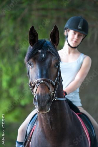 Portrait of black horse with teenage girl equestrian on it