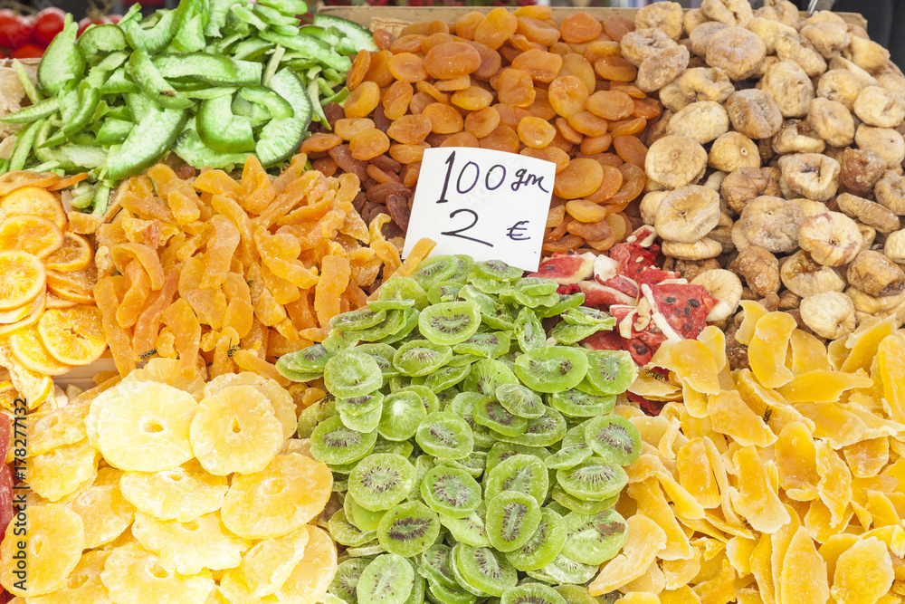Colorful display of sugared dried tropical fruit  on a street stall with kiwi, papaya, pineapple, peach, mango, banana, watermelon and several wasps attracted by the sugar
