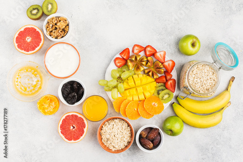 Fototapeta Naklejka Na Ścianę i Meble -  Healthy breakfast with oats, variety of fruits, strawberries, mango, grapes, figs, bananas and dates, yogurt and nuts served on the white table, top view, copy space for text, selective focus