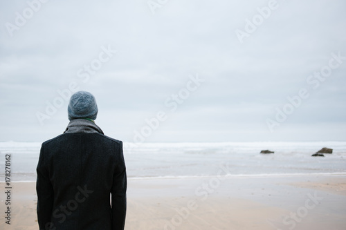Man standing alone on the beach looking out to sea photo