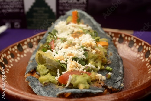 Mexican tlacoyos, a dish made with blue corn and filled with fried beans or broad beans, similar to mexican gordita, with guacamole, spicy sauce, coriander and cheese at the top