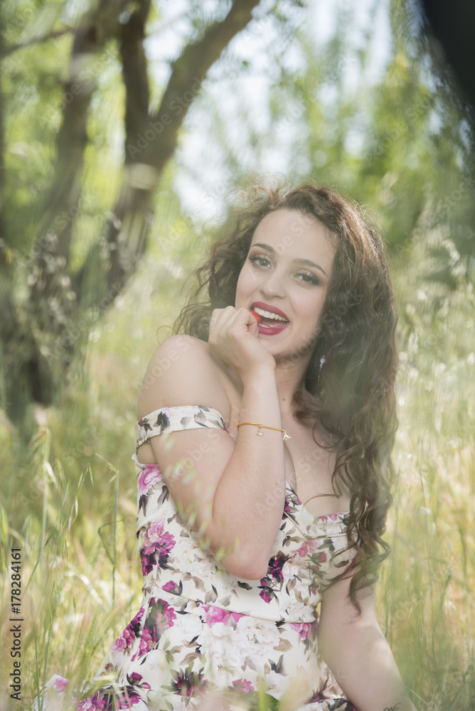 Sweet young woman sitting in dry field wearing a floral short dress eating cherry, outdoor vertical shoot Sweet young woman sitting in dry field wearing a floral short dress eating cherry, outdoor vertical shoot