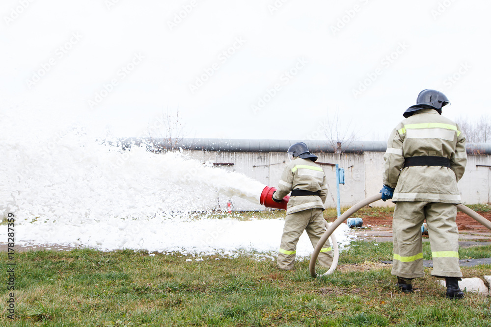 Obraz premium Firefighters extinguish the fire with a chemical foam coming from the fire engine through a hose
