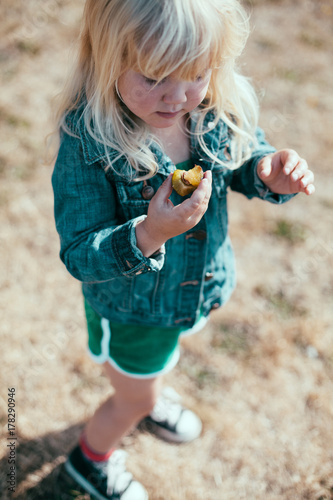 A little girl stands and eats a fresh plum.