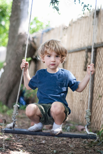 Child stands on an old wooden swing in his backyard photo