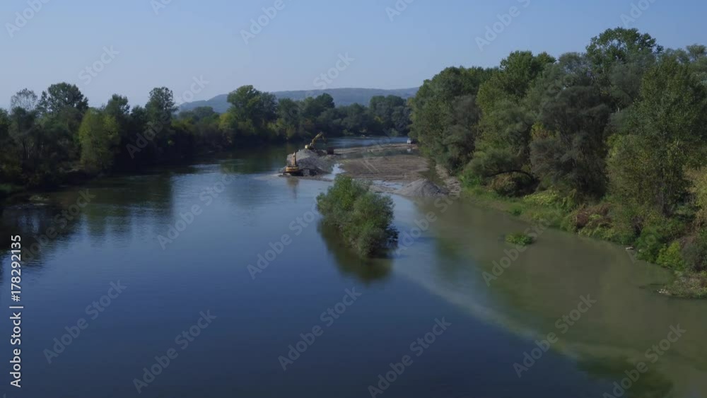 Aerial view of wide river flow, forest trees on riverbank , two yellow dredges shoveling sand, dump truck coming, excavators making pile on sandbank, drone flying and tracking mud on water surface Aerial view of wide river flow, forest trees on riverbank , two yellow dredges shoveling sand, dump truck coming, excavators making pile on sandbank, drone flying and tracking mud on water surface