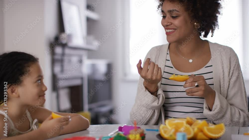 Young mother or childminder talking to two children as they eat a fruit snack