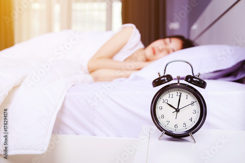 alarm clock on table and woman sleeping on bed in bedroom