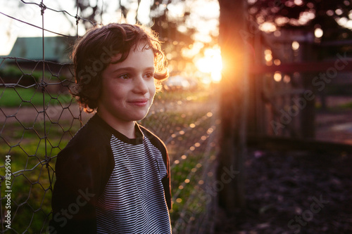 Boy standing against a fence at sunset