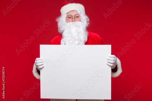 Santa Claus pointing in blank advertisement banner isolated on red background with copy space © satyrenko