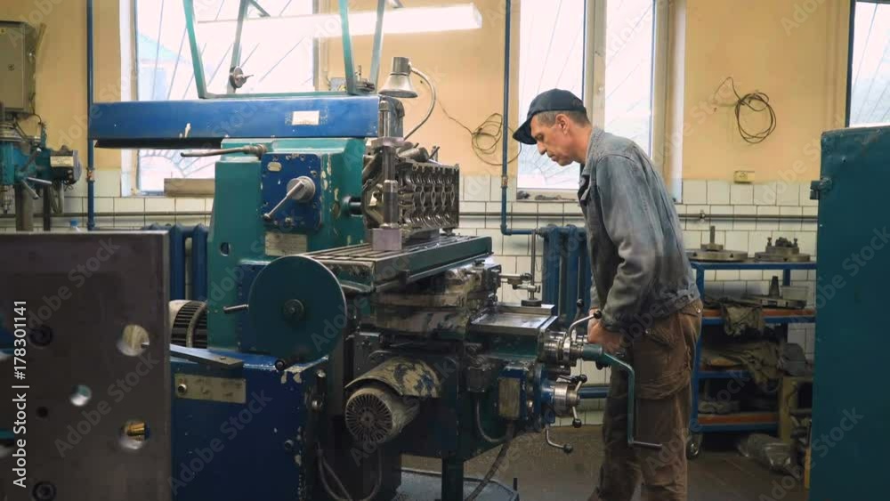 Mature caucasian man adjusting milling machine for milling of cylinder head in old shabby car service. Shot with Sony a7s and Atomos Ninja Flame, dolly slide.
