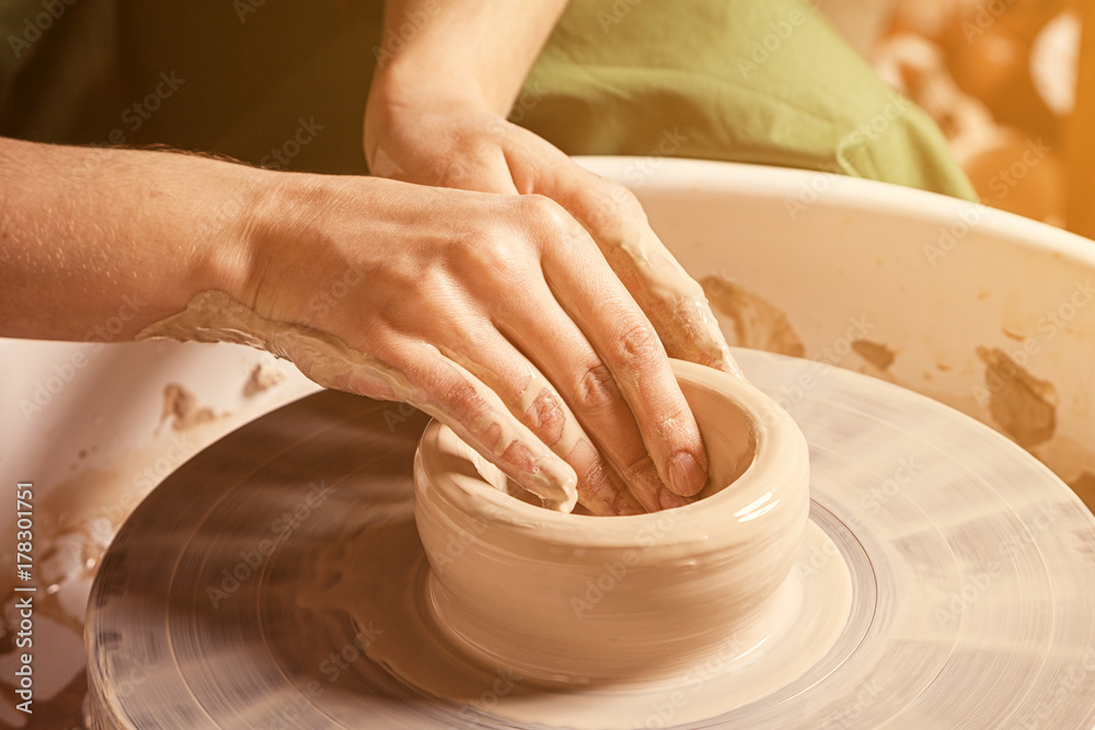 Close-up of a young woman potter beautifully sculpts a brown clay vase and makes for her neck on a potter's wheel, a top view