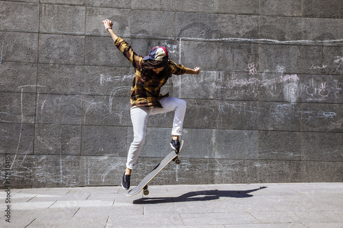 Young skater woman jumping with her skateboard in front dirty wall. photo