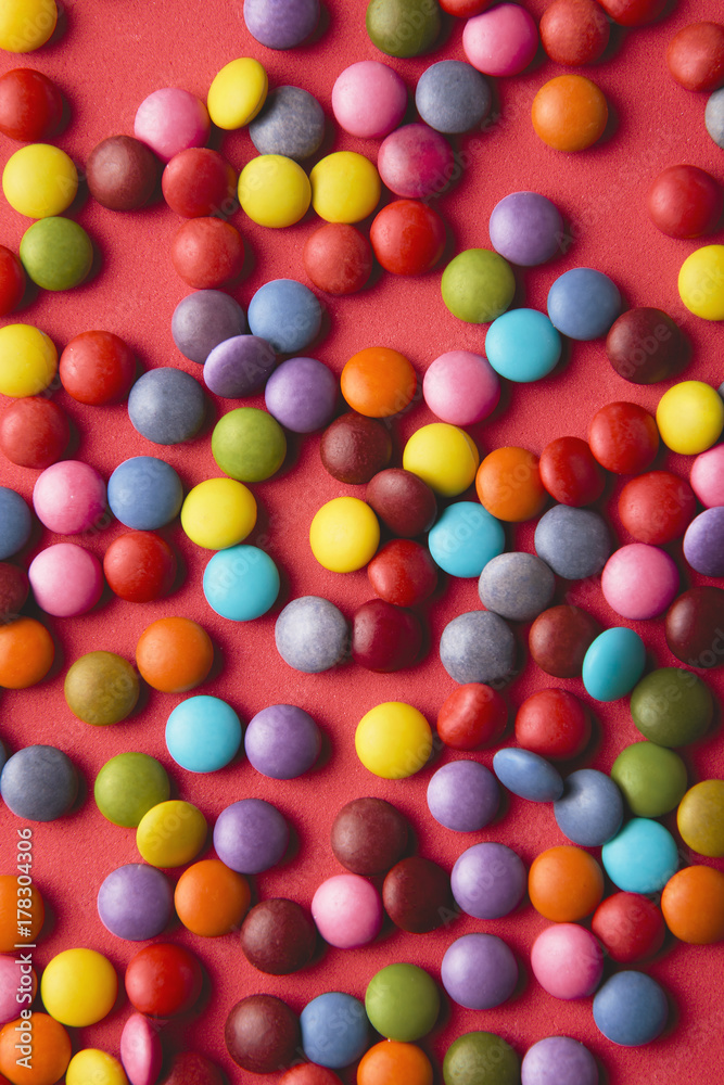 Close up of a pile of colorful chocolate coated candy on red background.