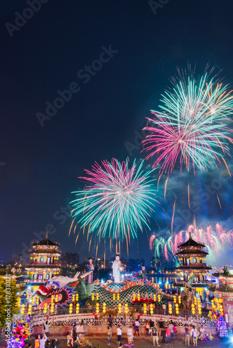 Fireworks at Lotus Pond behind Guanyin statue riding a dragon in the front end of the Spring and Autumn Pavilions opposite to Chi Ming Palace at night time with blue twilight sky in Kaosiung, Taiwan