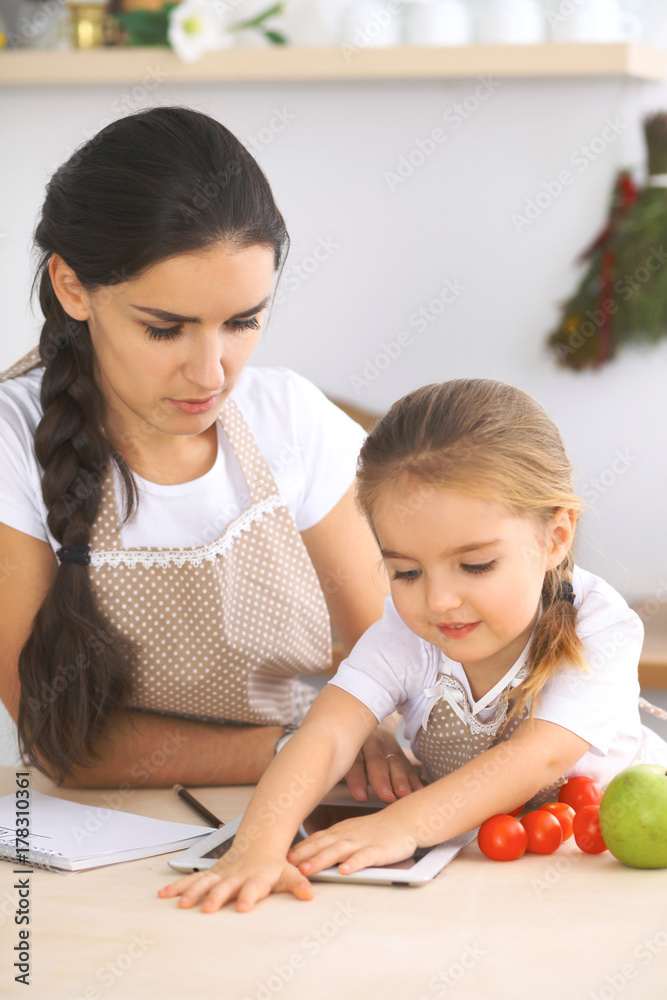 Happy family in the kitchen. Mother and child daughter make menue for cooking tasty breakfest in the kitchen. Little helper is ready for houshold job Happy family in the kitchen. Mother and child daughter make menue for cooking tasty breakfest in the kitchen. Little helper is ready for houshold job
