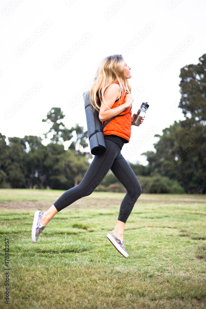 blonde woman in yoga blackyoga leggings jump with yoga mat and bottle of water in the park blonde woman in yoga blackyoga leggings jump with yoga mat and bottle of water in the park
