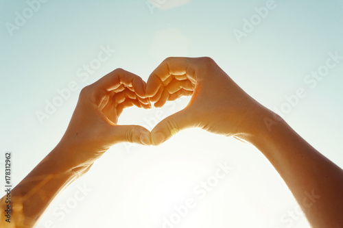 Close-up of woman's hand makes a heart shape against the sky photo
