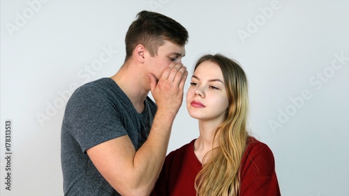 Foto Man whispering a secret to a surprised young woman on white background