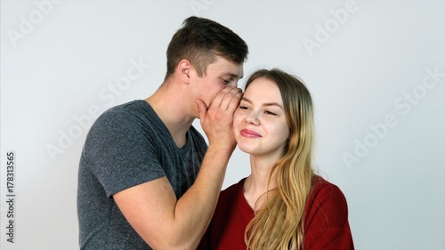 Billede på lærred Man whispering a secret to a surprised young woman on white background