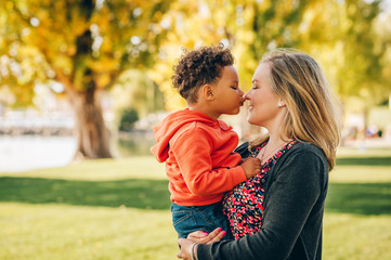 Happy young mother holding sweet toddler boy, family having fun together outside on a nice sunny day