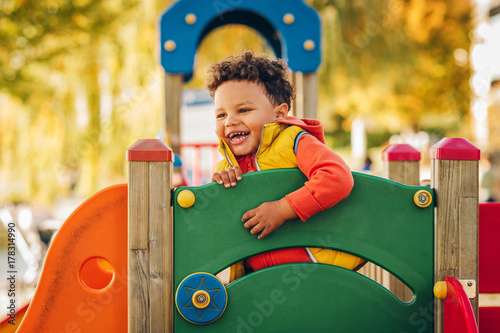 Adorable little 1-2 year old toddler boy having fun on playground, child wearing orange hoody jacket and yellow vest photo