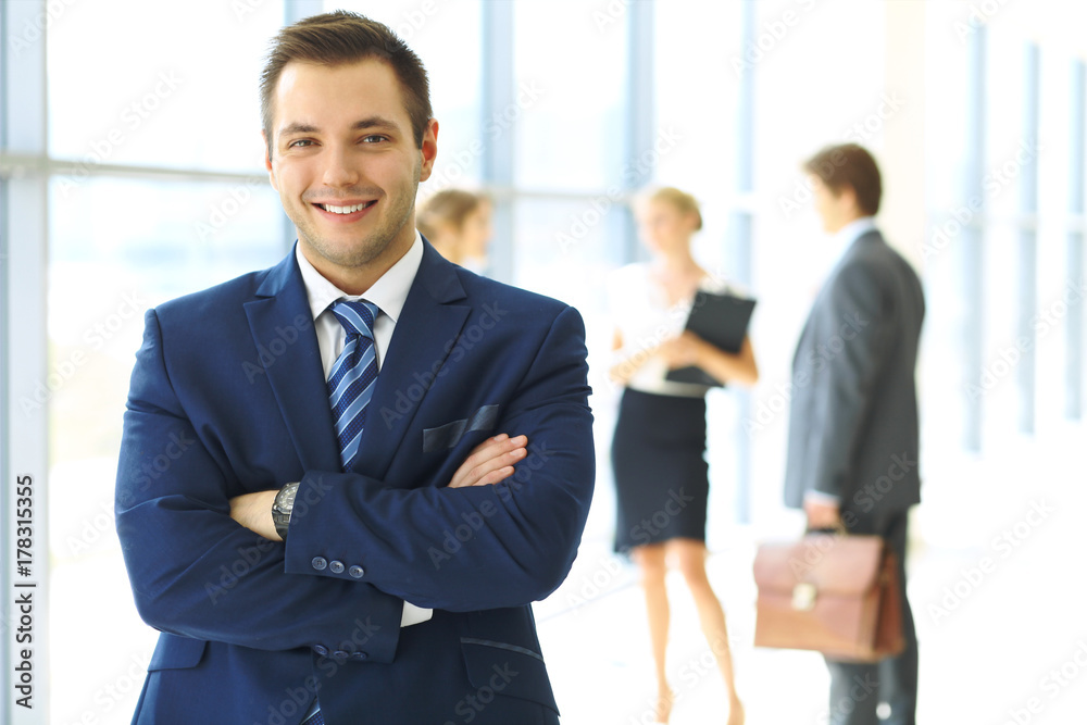 Smiling businessman in office with colleagues in the background Smiling businessman in office with colleagues in the background