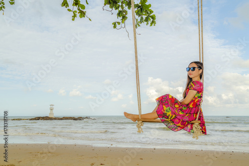 Asia women sit on wooden swing seat hanging on nice clean beach and deep blue sky