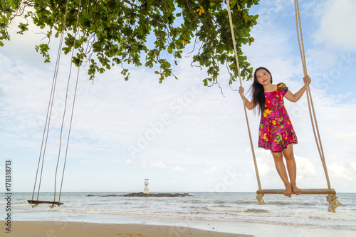Asia women on wooden swing seat hanging on nice clean beach and deep blue sky