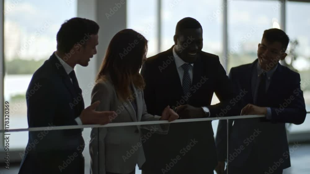 Tracking shot of young business lady and three businessmen standing, laughing and talking in hall of modern office building Tracking shot of young business lady and three businessmen standing, laughing and talking in hall of modern office building