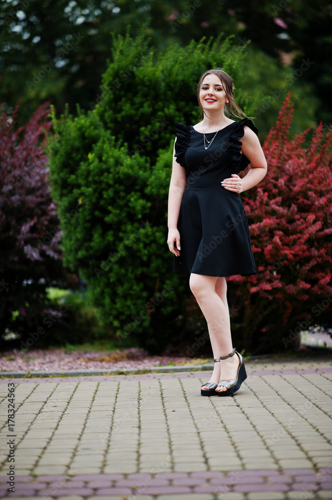 Portrait of a gorgeous young girl in black dress walking on the pavement in the park on a prom day. Portrait of a gorgeous young girl in black dress walking on the pavement in the park on a prom day.