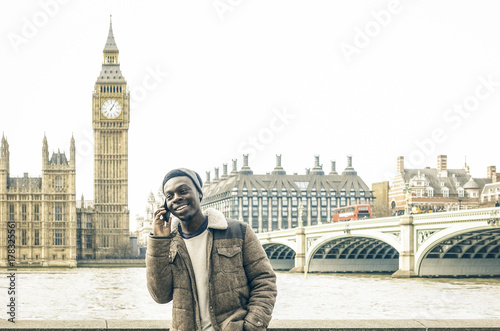 African american young man using mobile smart phone at Thames riverbank in London - Hipster guy male model with modern cell smartphone wearing trendy fashion clothes - Bright desaturated filter