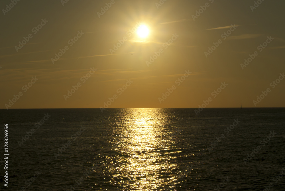 sunset or sunrise over the sea horizon, the sunny path and the silhouette of a sailboat