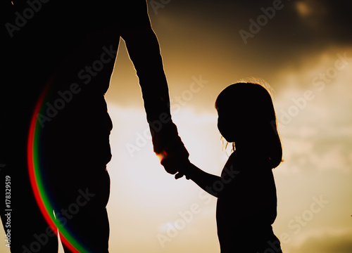 silhouette of little girl holding parent hand at sunset