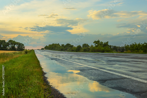 The road is asphalt after the rain at sunset. Reflection of clouds and sky in a puddle on the roadside. A calm evening look.
 photo