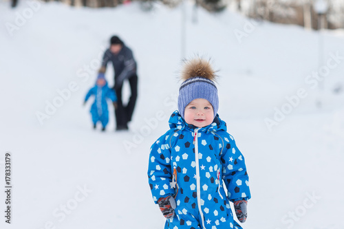 Portrait of cute boy twin in winter Park on background of his father and brother