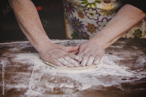 Old female baker kneading dough on wooden table