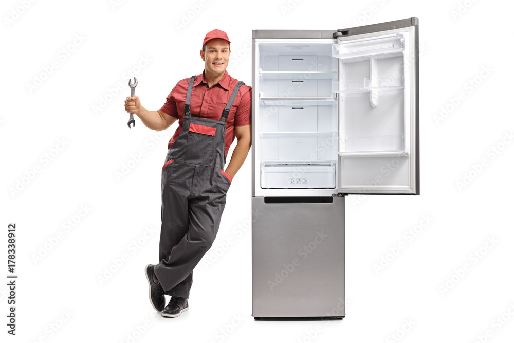 Repairman holding a wrench and leaning against an empty fridge