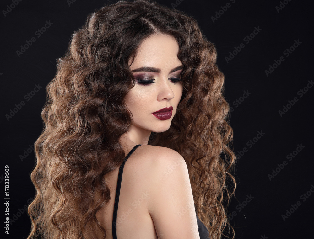 Fototapeta premium Beauty girl hair. Curly hairstyle. Brunette girl with healthy long hair, beauty makeup. Beautiful woman with marsala matte lips isolated on studio black background