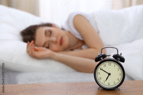 Beautiful sleeping woman resting in bed and trying to wake up with alarm clock