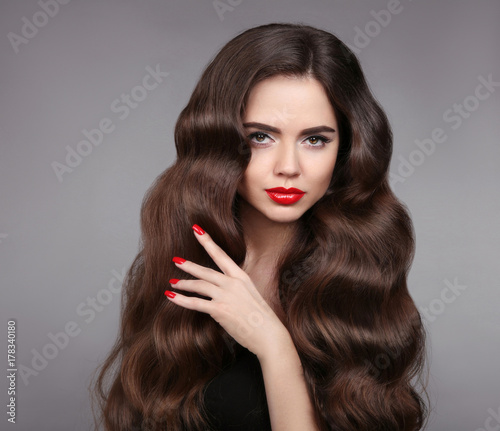 Beauty girl hair. Red lips and manicured nails. Beautiful model portrait with wavy hair and makeup isolated on studio grey background.