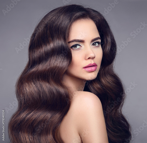 Beauty long wavy hair. Elegant Brunette girl portrait with healthy shiny hairstyle. Beautiful model with makeup isolated on studio dark background. Shampoo care product.