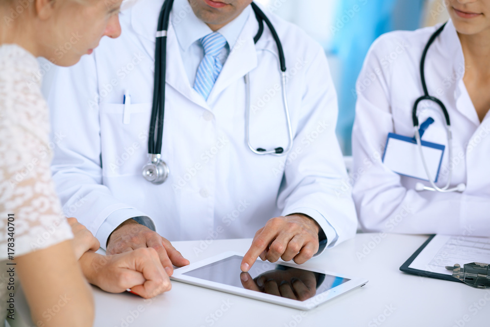 Doctor and patient talking while sitting at the desk in office. Physician pointing into touch pad computer or tablet. Medicine and health care concept Doctor and patient talking while sitting at the desk in office. Physician pointing into touch pad computer or tablet. Medicine and health care concept