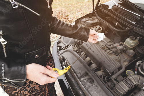 Girl opening the hood of her car checks the engine oil level