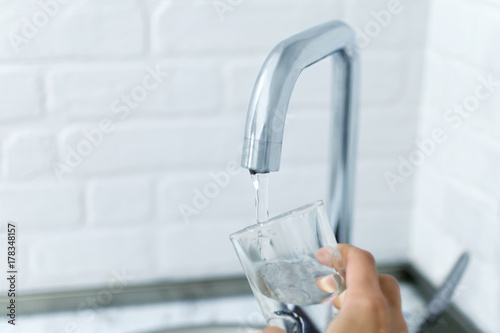 Hand holds the glass, filling it with water from the tap.